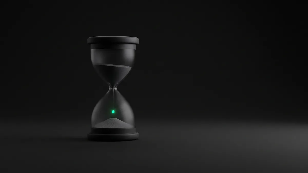 A matte-black hourglass alone on a dark seamless backdrop, one falling grain of sand glowing vivid emerald while the object sits in grayscale shadow